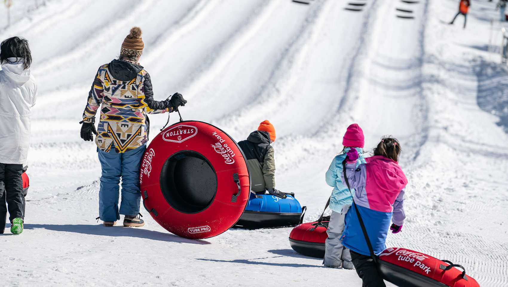 People with red and blue tubes stand on a snowy hill at a tubing park