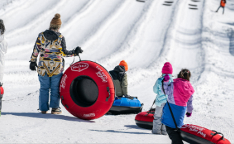 People holding large inflatable tubes at a snow tubing park with multiple snowy lanes